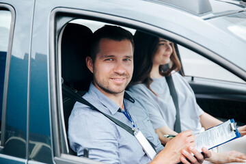 Driving school. Successfully passed test or exam. Male instructor loves his job and is happy to teach students. Man smiling and looking at camera. Blurred female student on background.