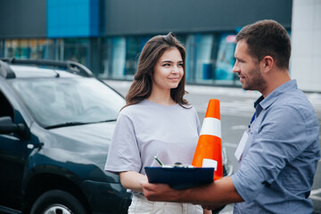 Female student of driving school signs instructor's papers and looks at him with interest. Orange...