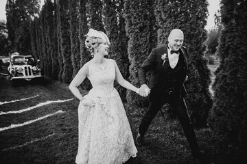 Newly married couple running and jumping in park while holding hands