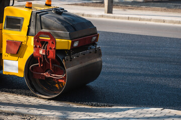 Asphalt road roller with heavy vibration roller compactor press new hot asphalt on the roadway on a road construction site. Heavy Vibration roller at asphalt pavement working. Repairing.