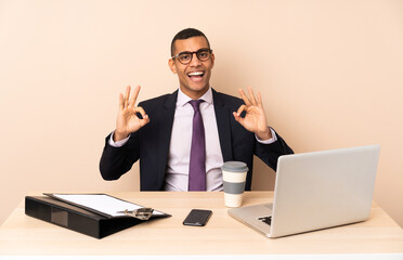 Young business man in his office with a laptop and other documents showing an ok sign with fingers