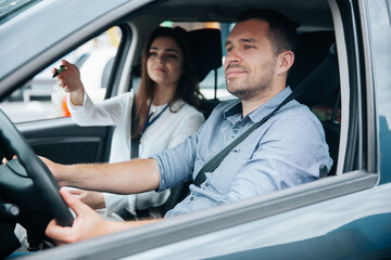 Female driving instructor pointing at object on road by her hand. Diligent male student driving the...