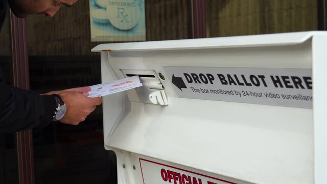 Young Man Drops Mail-in Ballot Letter in Slot at Official Voting Box with Drop Ballot Here Sign