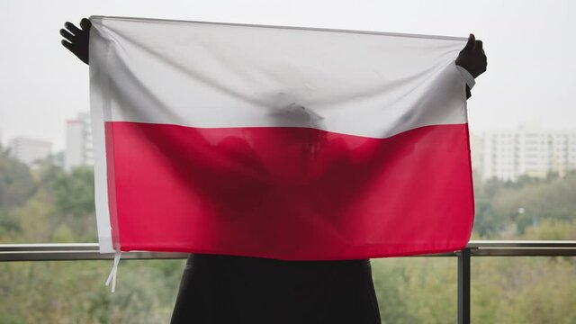 Black African Businessman Standing On The Balcony Holding And Raising Polish Flag At Daytime. - medium shot