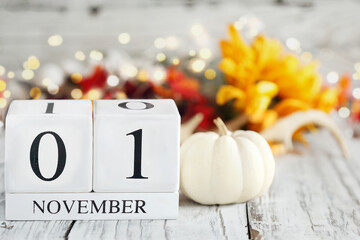White wood calendar blocks with the date November 1st and autumn decorations over a wooden table. Selective focus with blurred background. 
