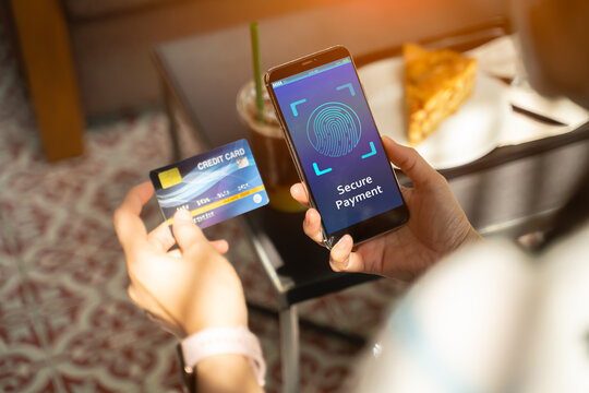 Secure payment,touch id scan,fingerprint id and data credit card protection concept.Woman hands using mobile phone and holding credit card in coffee shop.