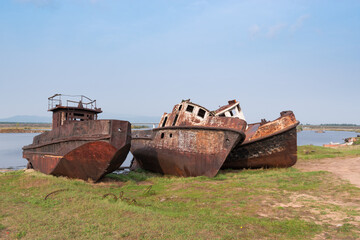 Fototapeta na wymiar Rusty metal hulls of river vessels stand on the banks of the Barguzin River near the Barguzinsky Bay of Baikal, the largest freshwater lake in the world. 