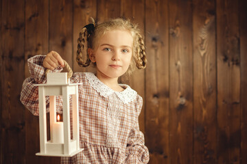 Little child girl holding a lighted lamp with a candle in her hands
