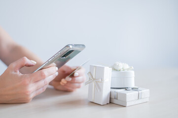 A faceless woman sits at a table and holds a mobile and a credit card in her hands. Online shopping for gifts concept