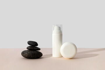 Fototapeta na wymiar Bottles of cosmetic cream with balancing stones on beige background in sunlight