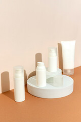 Bottles of cosmetic cream on podium over brown background in sunlight