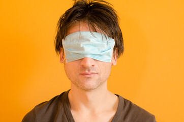 Tired man with mask on his eyes, not protect him from virus, on yellow background, put on mask...
