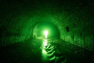 Bright green light in the tunnel of the sewer drainage of an old brick collector in the shape of a...