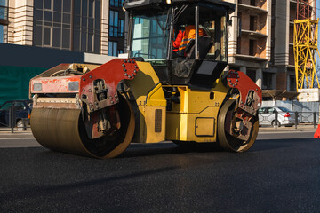 Naklejka premium Asphalt road roller with heavy vibration roller compactor press new hot asphalt on the roadway on a road construction site. Heavy Vibration roller at asphalt pavement working. Repairing.