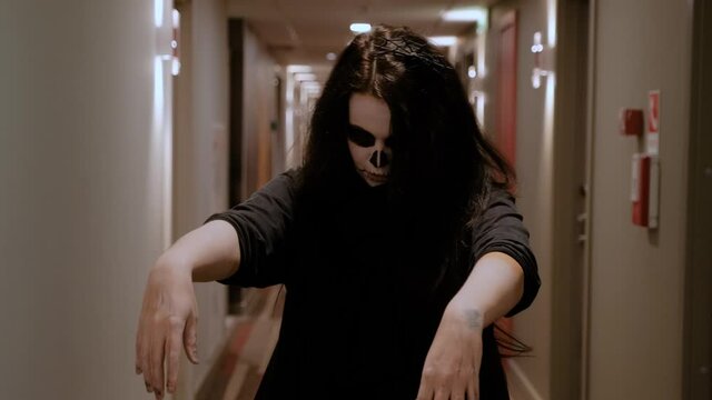 A girl with long hair in the form of a zombie slowly approaches the camera, stretching out her pale arms. Halloween Eve. October holiday. Festive humor.