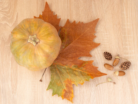 Orange pumpkin on a large maple autumn leaf on a wooden table