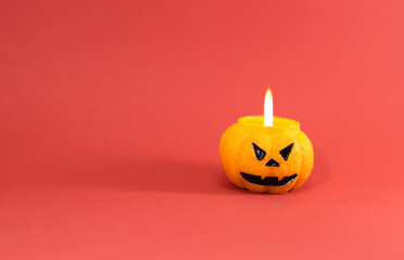 One scary orange pumpkin shaped candle with a fire, isolated on red background, space for text. Tradition Happy Halloween concept.