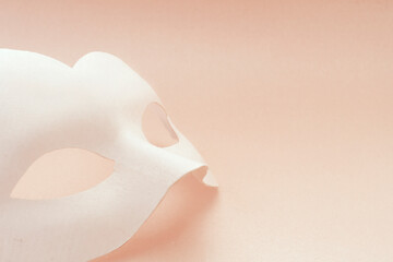 White carnival mask on a pink background. The mask lies vertically.