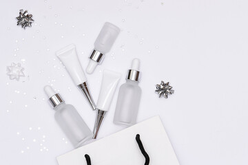 Set of skin care cosmetic creams and serums in white paper bag on white background with silver sparkling decorations. Christmas cosmetic sale. 