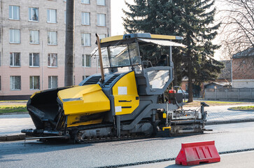 Industrial asphalt paver machine laying fresh asphalt on road construction site on the street. A Paver finisher placing a layer of a new hot asphalt on the roadway on a construction site. Repairing.