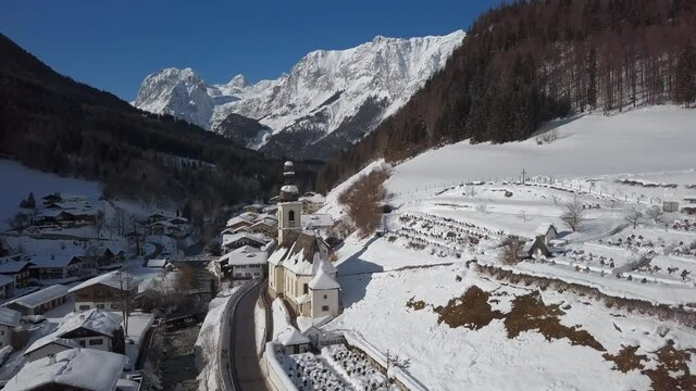 Winter flight over Ramsau town and famous Parish church St. Sebastian, Berchtesgaden, Bavarian Alps, Germany