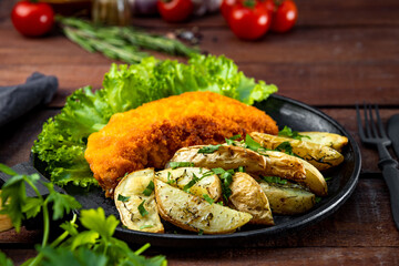  Pork schnitzel with baked potatoes in a pan on a wooden table close-up
