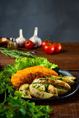  Pork schnitzel with baked potatoes in a frying pan on a wooden table close-up, vertical photo