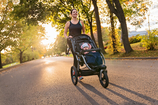Beautiful young mother with her daughter in jogging stroller running outside in autumn nature