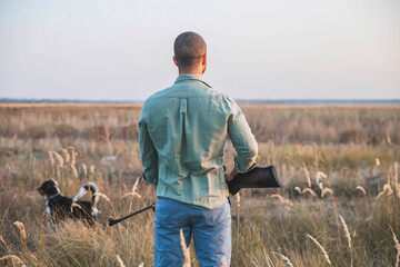 Hunter with a gun and a dog stands in the field