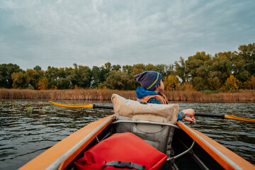 Fototapeta premium Evening kayak trip along the river in autumn. The active lifestyle of the child in the family.