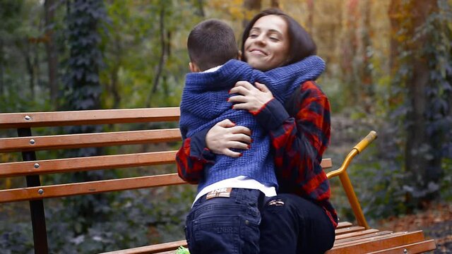 Young preschooler kid kiss his happy mother at her nose on a bench at the park at warm autumn day