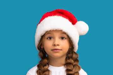 A little girl in a Christmas hat poses on a blue background.