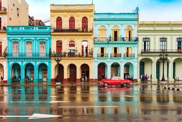 red classic car in front of colorful houses in old havana on a rainy day