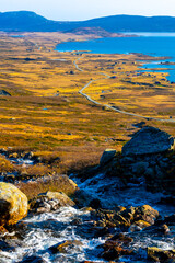 Small stream flowing down into a large lake with cabins around it in the mountains in Norway.
