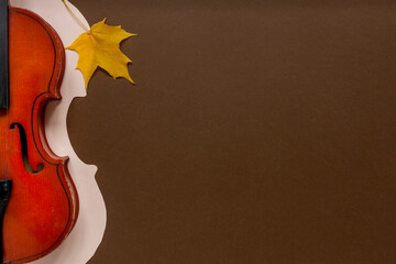Old violin on light paper background with paper cut violin silhouette and maple autumn leaf. Top...