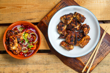 Plates of pan-Asian salad with sesame seeds and grilled chicken in yakitori sauce on wooden stands and loya food sticks.