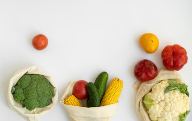 Vegetables in eco bag on white surface with a copy space. Pepper, tomato, corn, cucumber, broccoli, cauliflower in reusable shopping eco friendly cotton fabric bags. Zero waste plastic free concept.