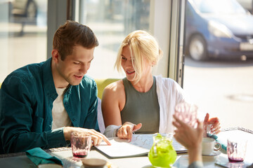 young caucasian couple is choosing meal in menu together, blonde beautiful woman and handsome guy sit talking, sharing opinions