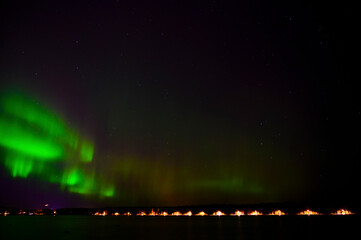 Green Aurora borealis beam of northern lights with purple tail beside a lake under starry sky with...