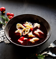 Christmas Eve borscht with the addition of dumplings with mushrooms filling in black bowl. Traditional Christmas Eve soup in Poland