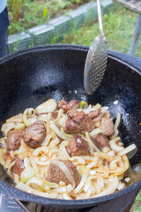 Cooking pilaf in a cauldron on the grill outside in the summer