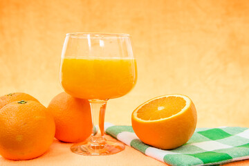 Una copa de zumo de naranja, naranjas sobre la mesa
