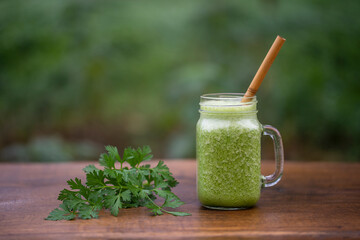 Green smoothie of parsley, avocado, honey and banana in a glass mug on a wooden table in a garden cafe, close-up