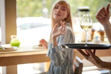 glad waiter bring glass of champagne on tray to customers, treats women in restaurant. caucasian woman is thankful for service. focus on glass with beverage