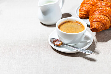 Croissants and cup of coffee in the morning light, sunlight shadow, on a linen fabric. Morning breakfast concept.