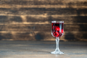 Homemade tincture of red cherry in a wine crystal glass on wooden background, Ukraine