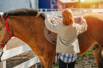 Routine of ginger girl preparing her horse for the ride, putting on saddle pad.
