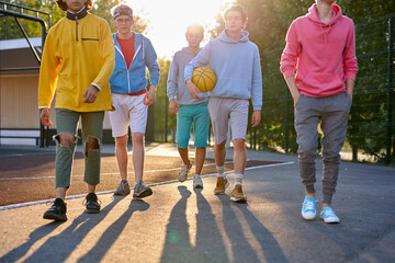 Naklejka premium sportive young boys going to play basketball in the street, handsome teenagers have friendly talk while they are going at playground