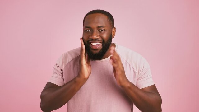 Playful african american man preening his beard, winking to his mirror reflection at camera, pink background