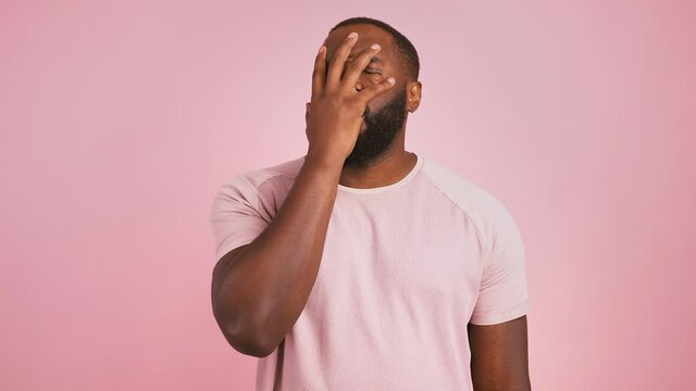 Disappointed stressed guy covering face with hand over pink studio background
